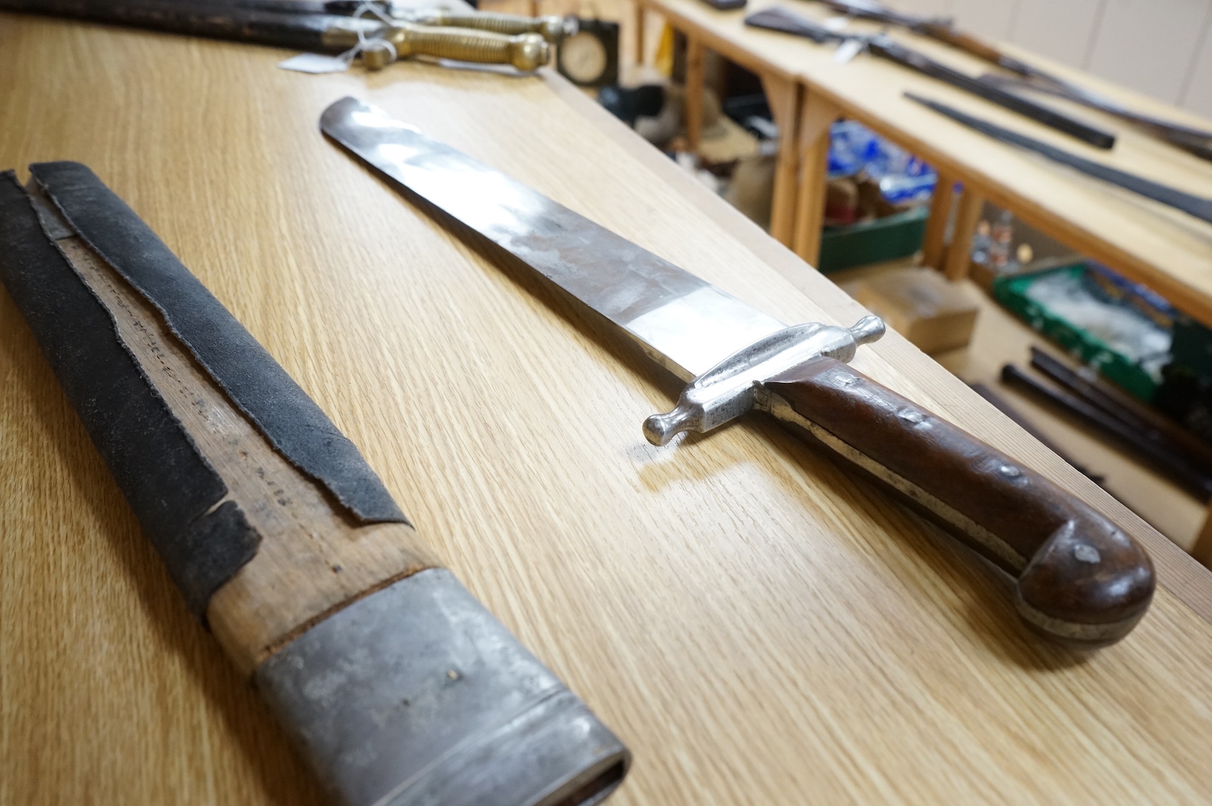 A 19th century Austrian military fascine knife, regulation iron crosspiece, two piece riveted wooden grips, in its wooden scabbard with iron mounts, leather covering loose
